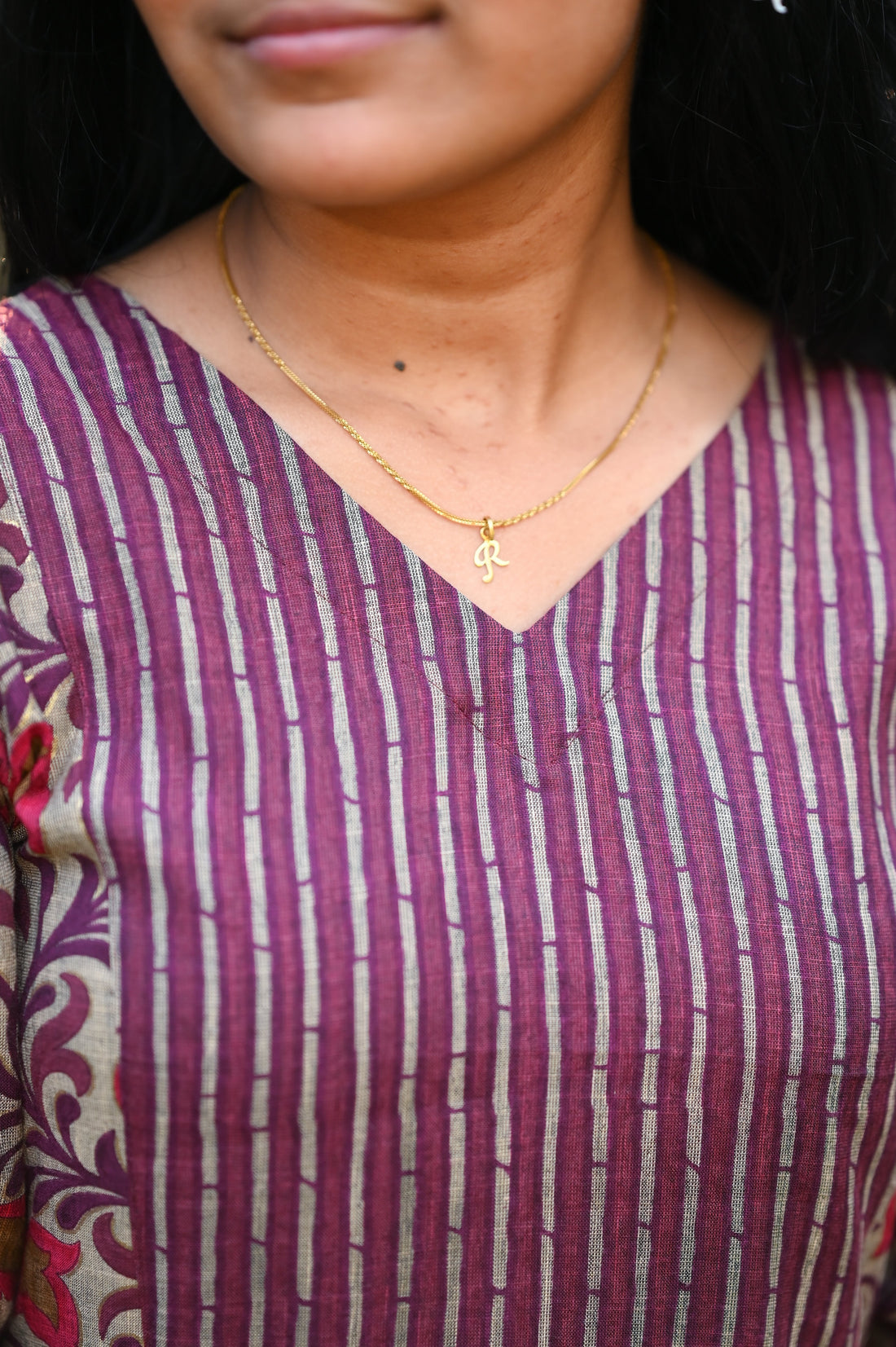 Woman wearing a maroon and white striped top with a gold necklace.